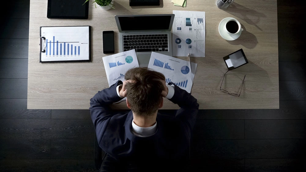 Sad businessman sitting at table and thinking about debts, bankruptcy, top view
